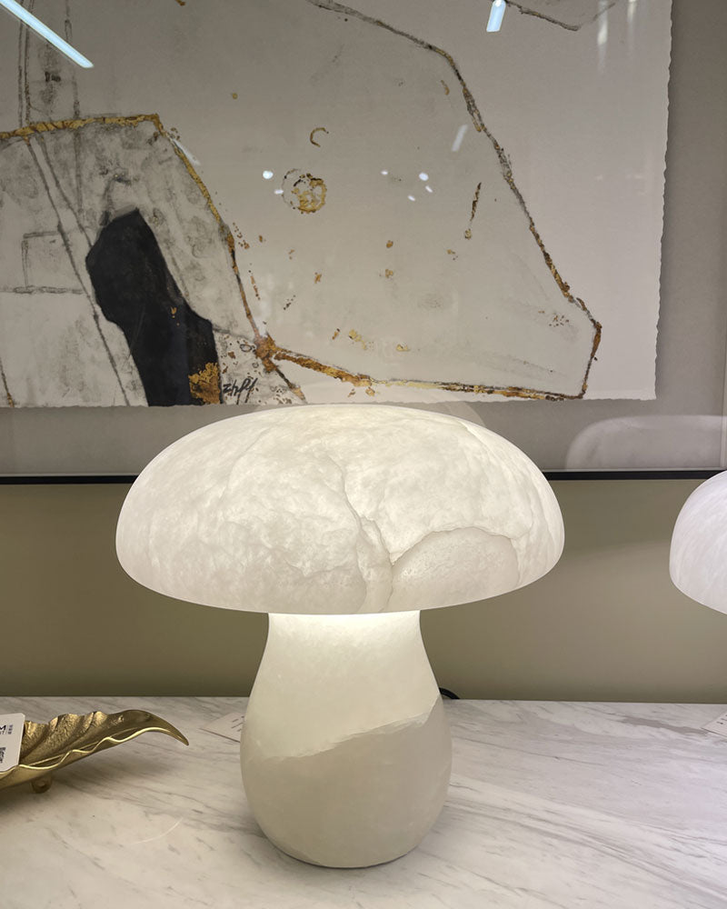 Mushroom-shaped lamp on marble table, softly glowing in front of abstract wall art.