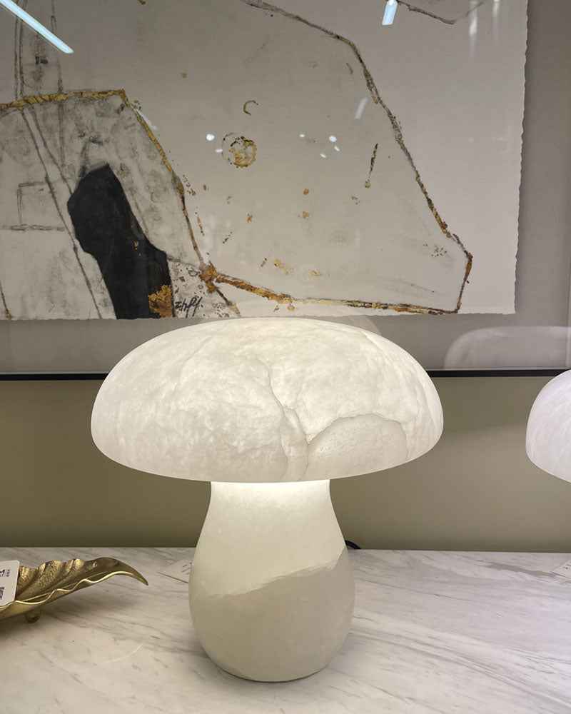 Mushroom-shaped lamp on marble table, softly glowing in front of abstract wall art.
