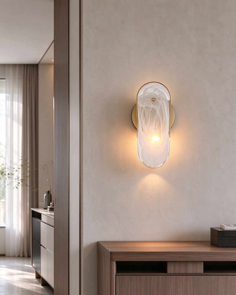 A modern wall-mounted light fixture with a frosted white glass shell and warm glowing bulb, installed on a beige wall above a wooden console table in a minimalist interior.