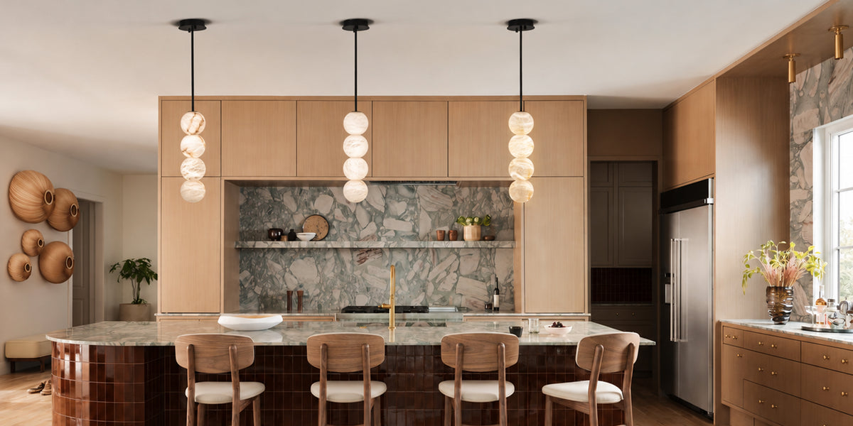 A modern kitchen interior with light wood cabinetry, a stone backsplash, a central island with bar stools, and three hanging pendant lights with stacked frosted glass spheres.