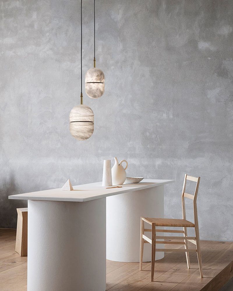 Minimalist alabaster pendant lights over a modern white table with a ceramic pitcher