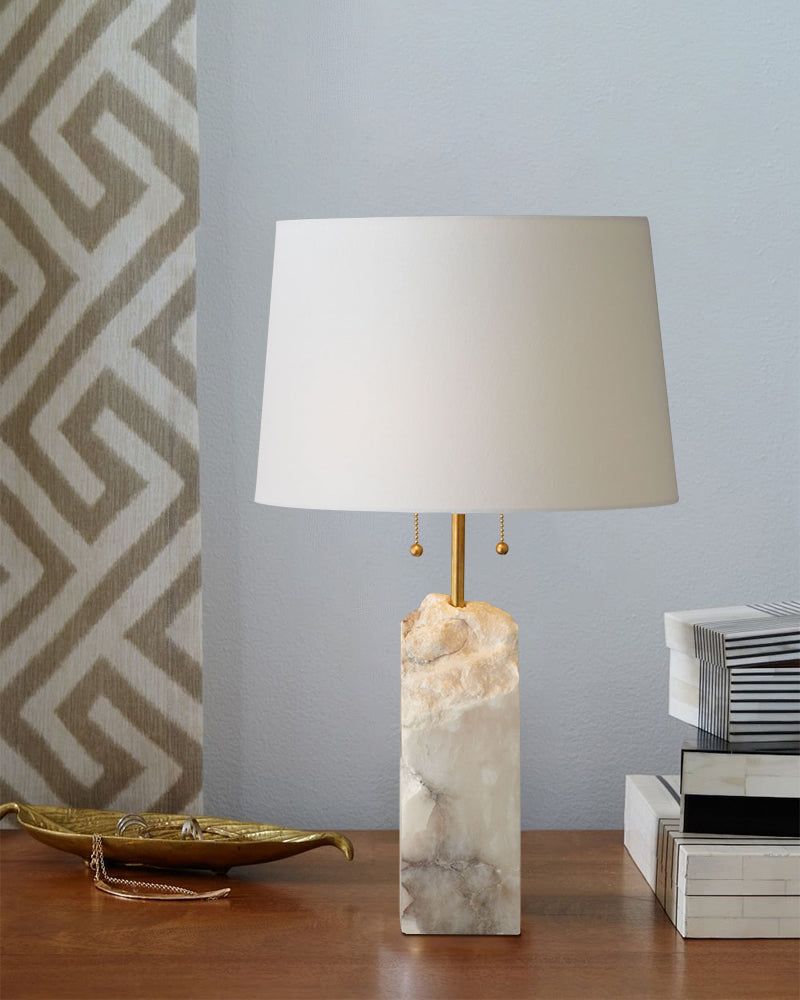 15" white alabaster table lamp with linen shade on wooden table near geometric wallpaper