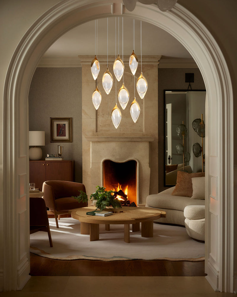 A modern multi-light pendant chandelier with teardrop-shaped frosted glass shades and warm gold-toned accents, hanging in a luxurious living room viewed through a large white archway.