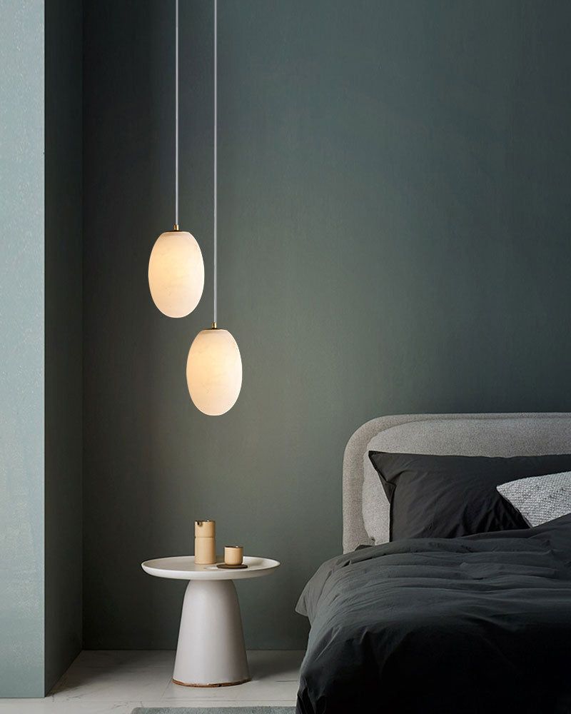 Two alabaster pendant lamps above a modern bed with black bedding in a serene bedroom.