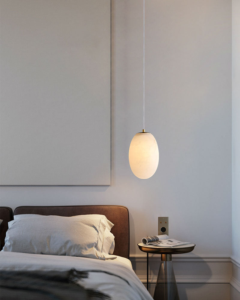 Sleek alabaster pendant lamp over a modern bed and nightstand in minimalist bedroom.