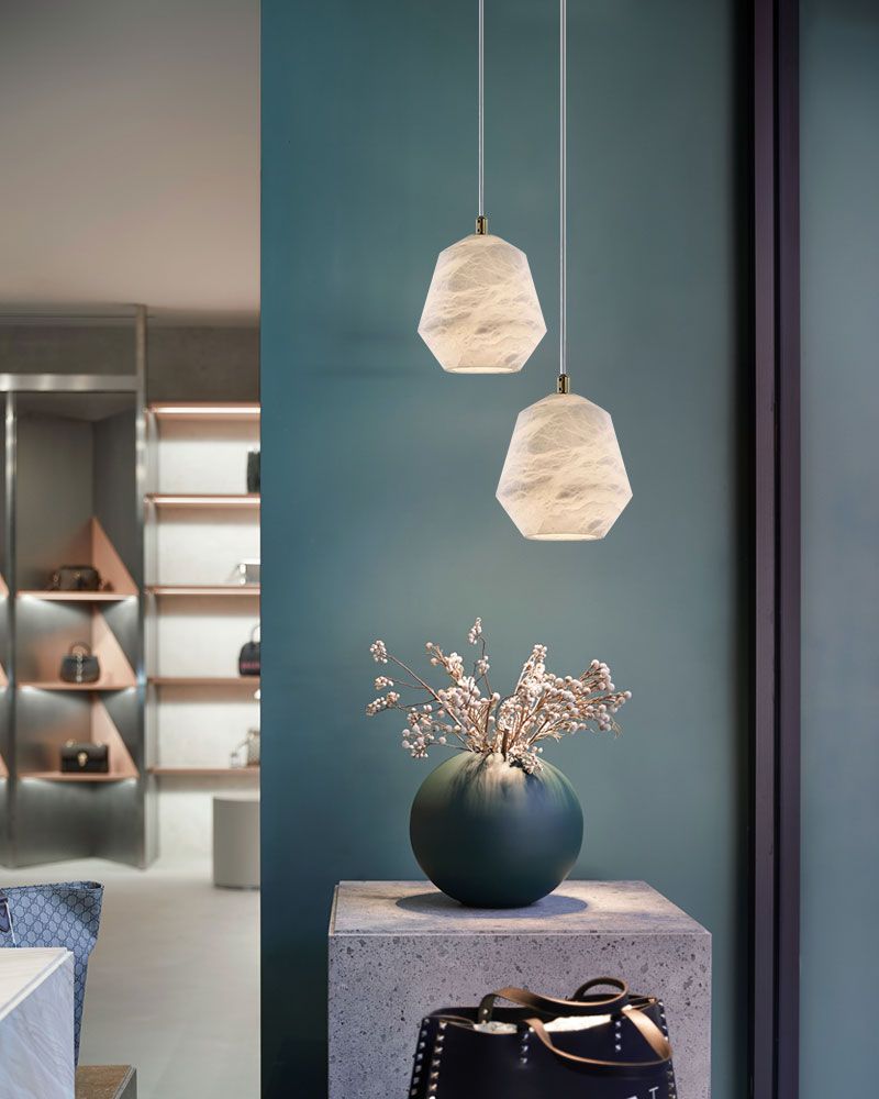 Hexagonal alabaster pendant lamps above decorative pedestal with vase in modern space.