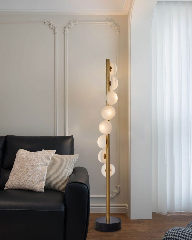 Brass skinny floor lamp with alabaster globes beside black sofa in contemporary room