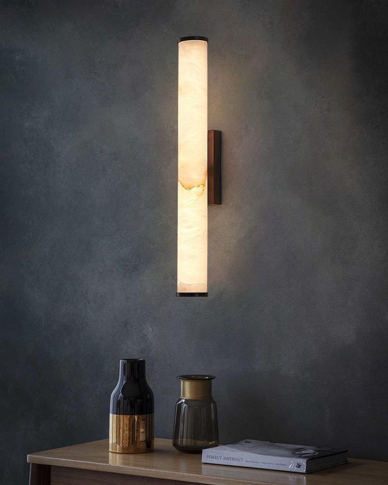 Elegant cylindrical alabaster wall sconce lamp illuminated above a stylish wooden table