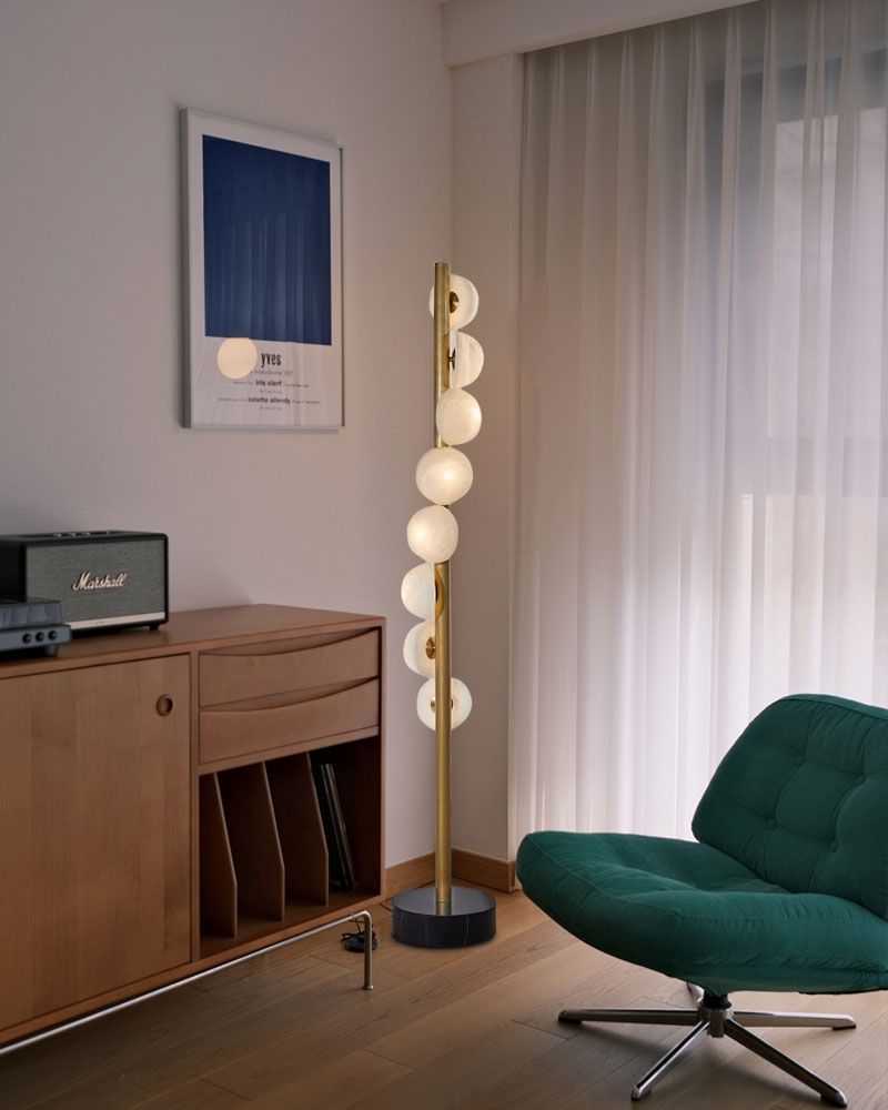 Modern brass floor lamp with alabaster globes in stylish room corner by green chair