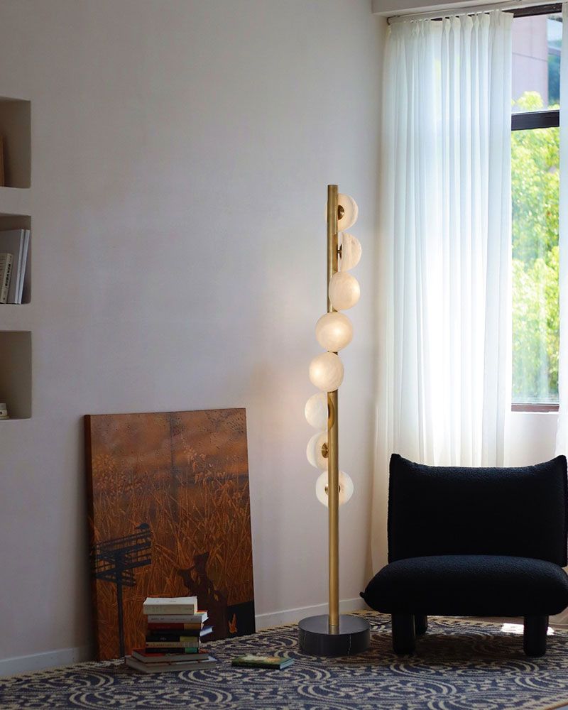 Modern vertical brass floor lamp with alabaster globes beside a black textured chair
