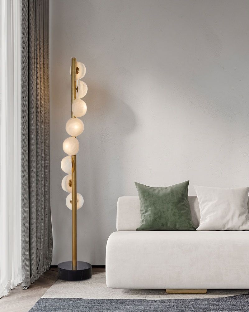 Modern vertical brass floor lamp with alabaster globes beside minimalist sofa