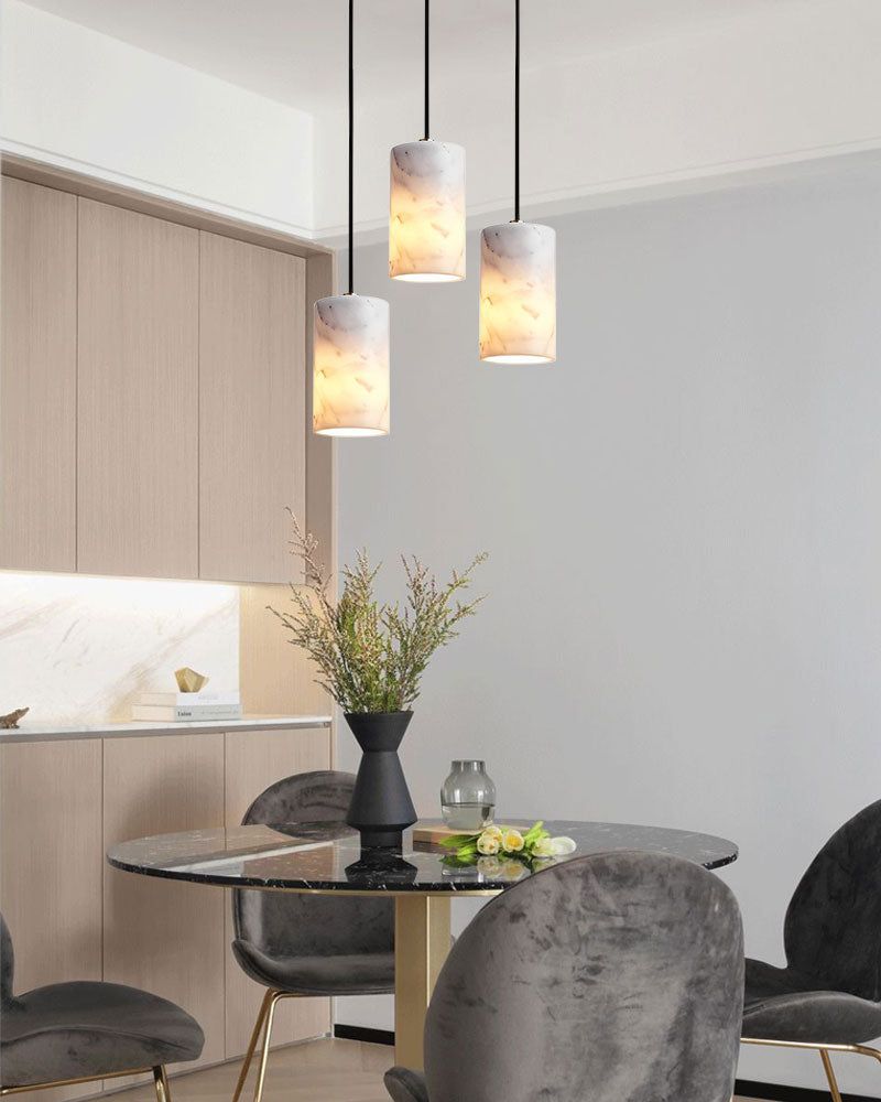Marble cylinder pendant lamps over a modern glass dining table with gray chairs.