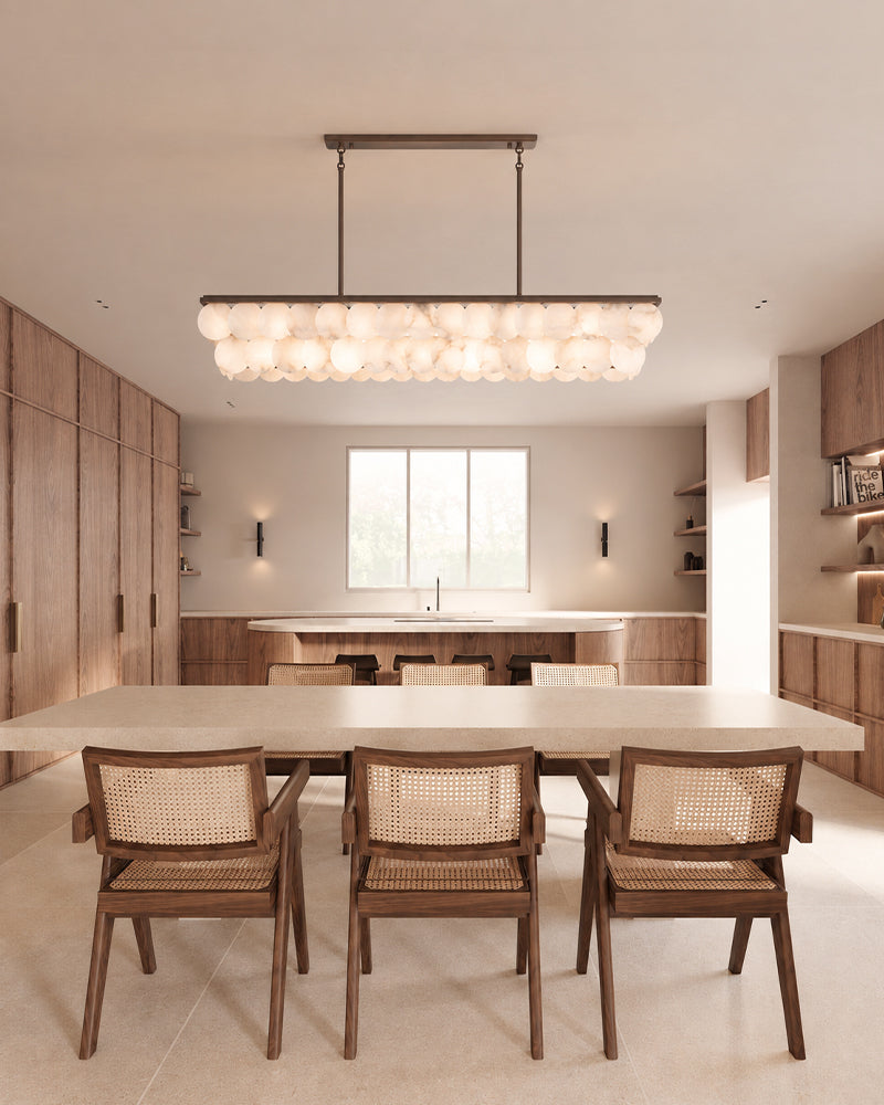 A modern rectangular linear pendant light with a cluster of glowing glass globes, suspended over a dining table with four wooden chairs in a warm, contemporary dining room.