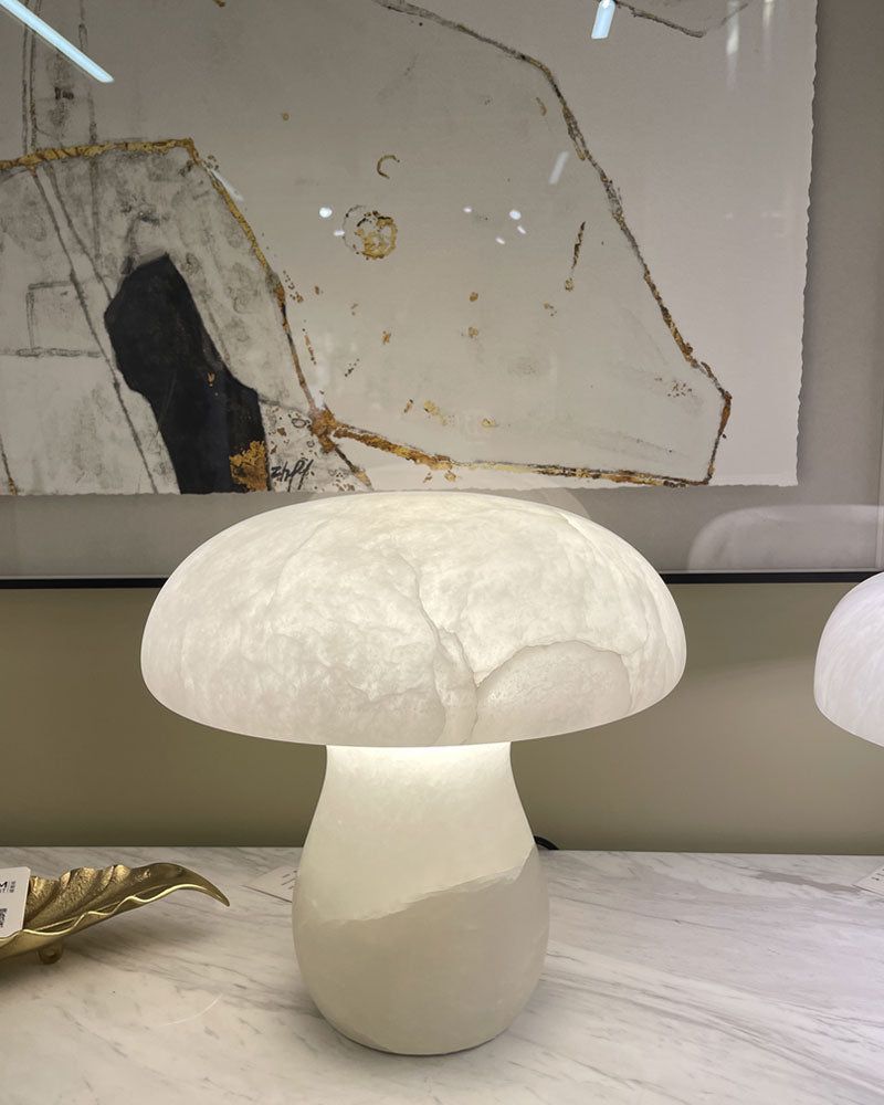 Mushroom-shaped lamp on marble table, softly glowing in front of abstract wall art.