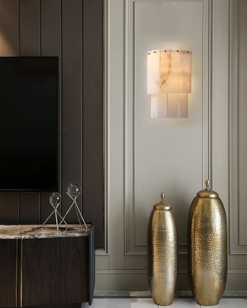 Marble wall sconce illuminating elegant living room with gold vases.