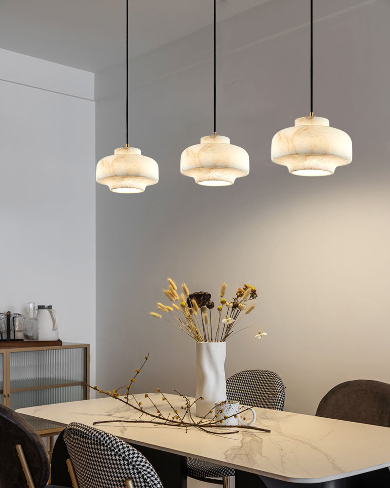 Three vintage alabaster pendant lamps above a modern dining table with floral centerpiece.