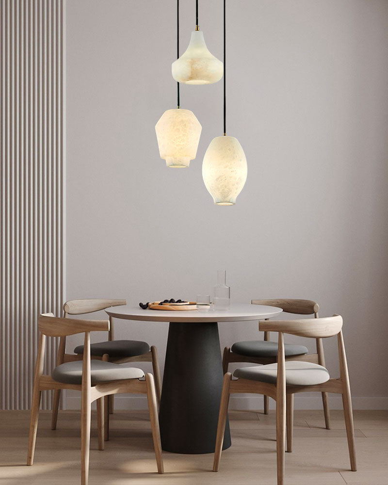 Three alabaster pendant lamps above a round dining table in a minimalist interior design.