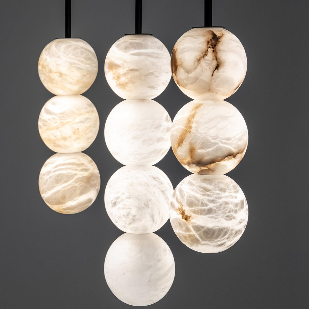 A cluster of hanging spherical pendant lights made from polished white and cream onyx stone, showing natural marbled patterns, suspended against a dark gray background.