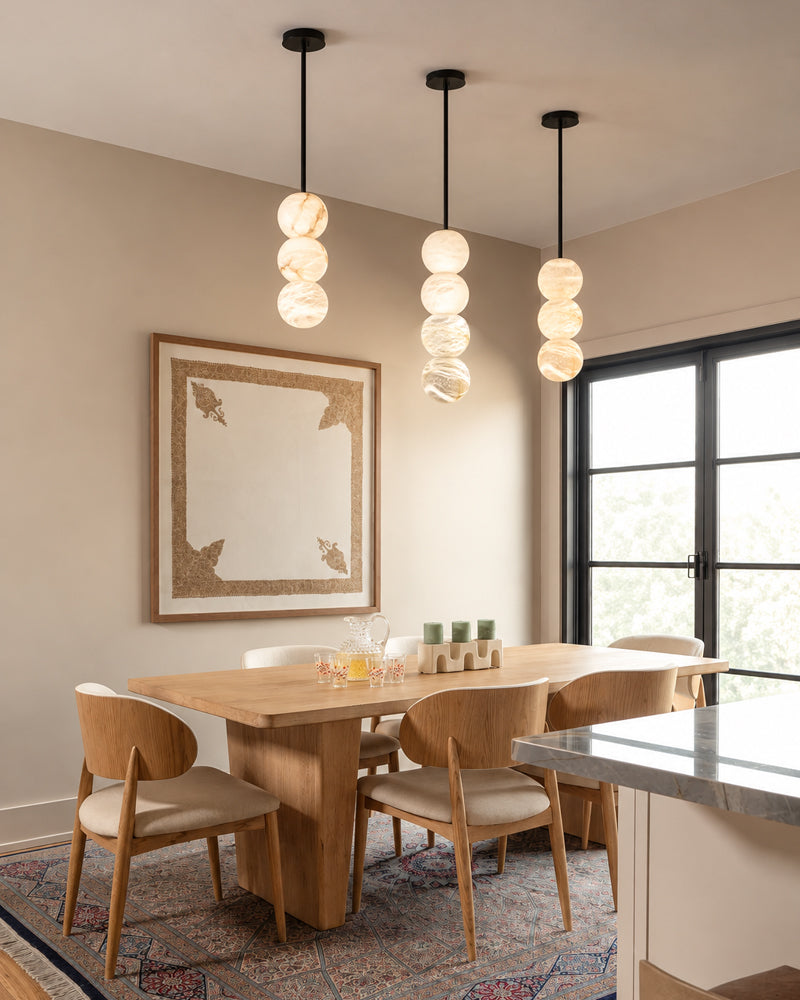 Three modern pendant lights with stacked spherical glass shades hang over a wooden dining table and chairs in a bright, contemporary dining room.