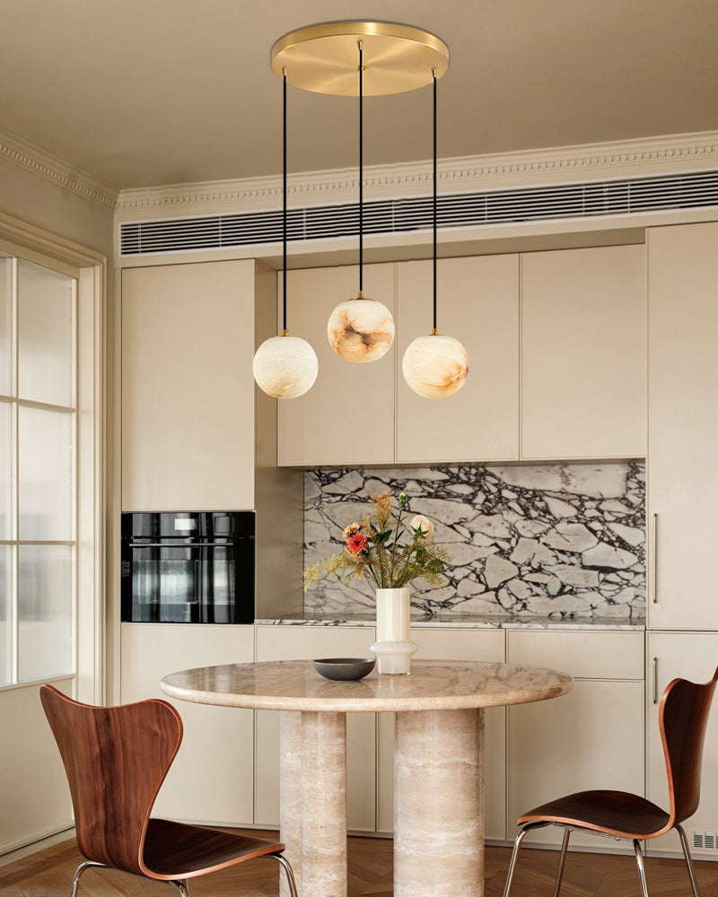 Cluster of three marble pendant lamps over round marble dining table in modern kitchen