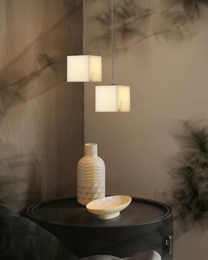 Square white alabaster pendant lights illuminating a modern side table with decorative vase.