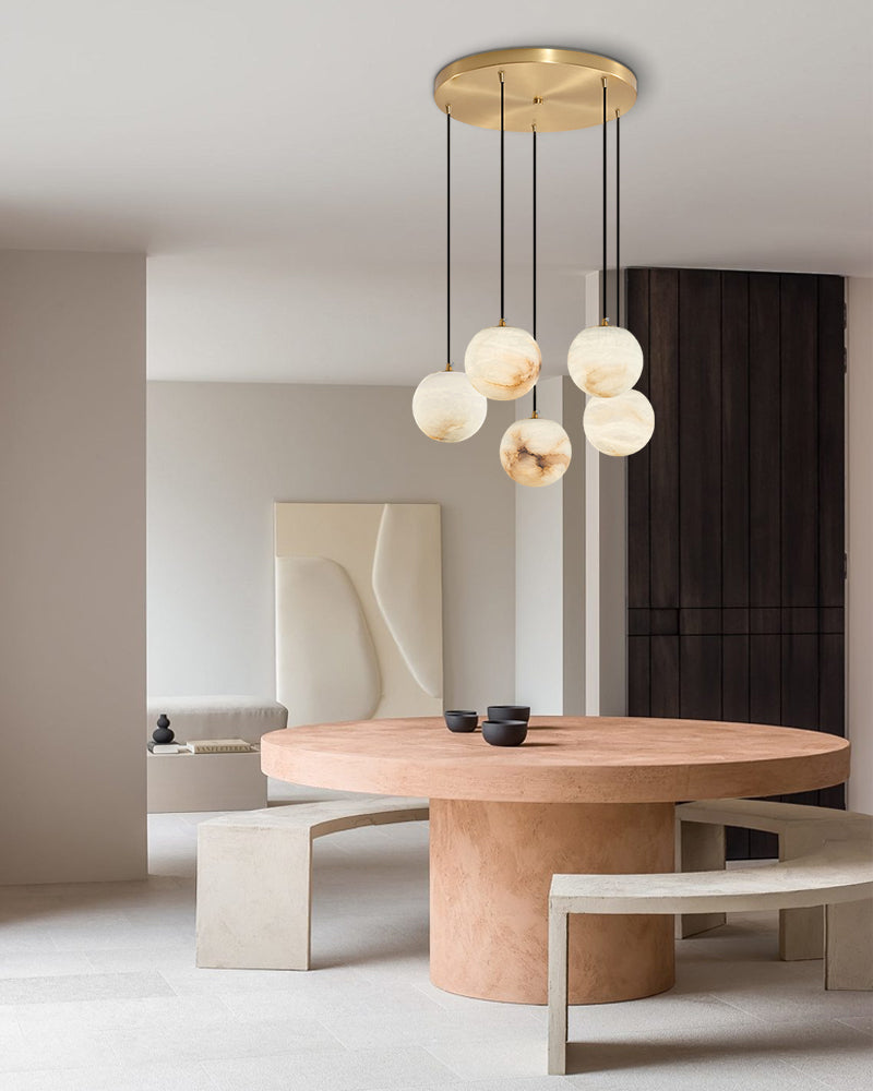 Chic marble pendant lamp cluster over a round peach dining table in a minimalist space.