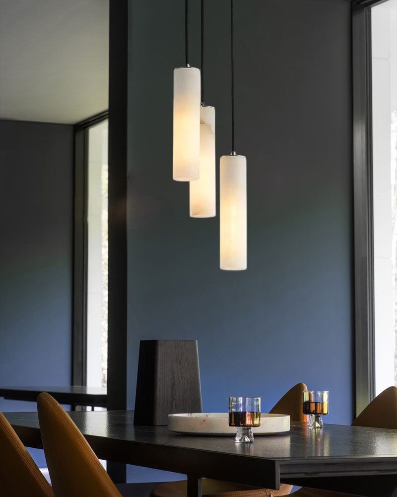 Three alabaster pendant lamps over a modern dining table with drinks