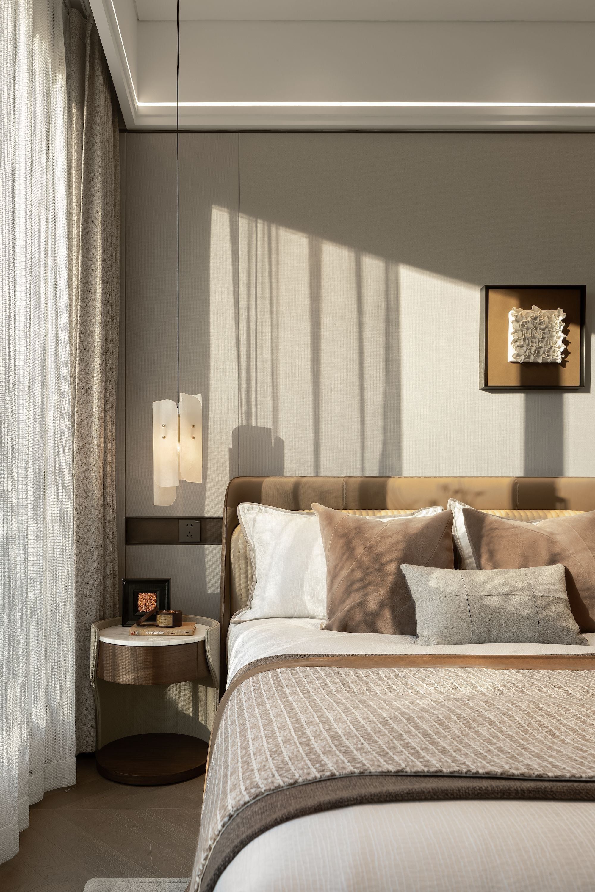 Elegant bedroom with beige bed, decorative cushions, and warm natural light.