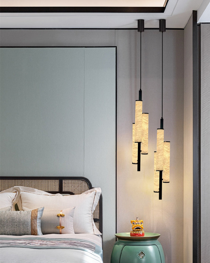 Three cylindrical alabaster pendant lamps hanging above a bedside table in a modern bedroom.