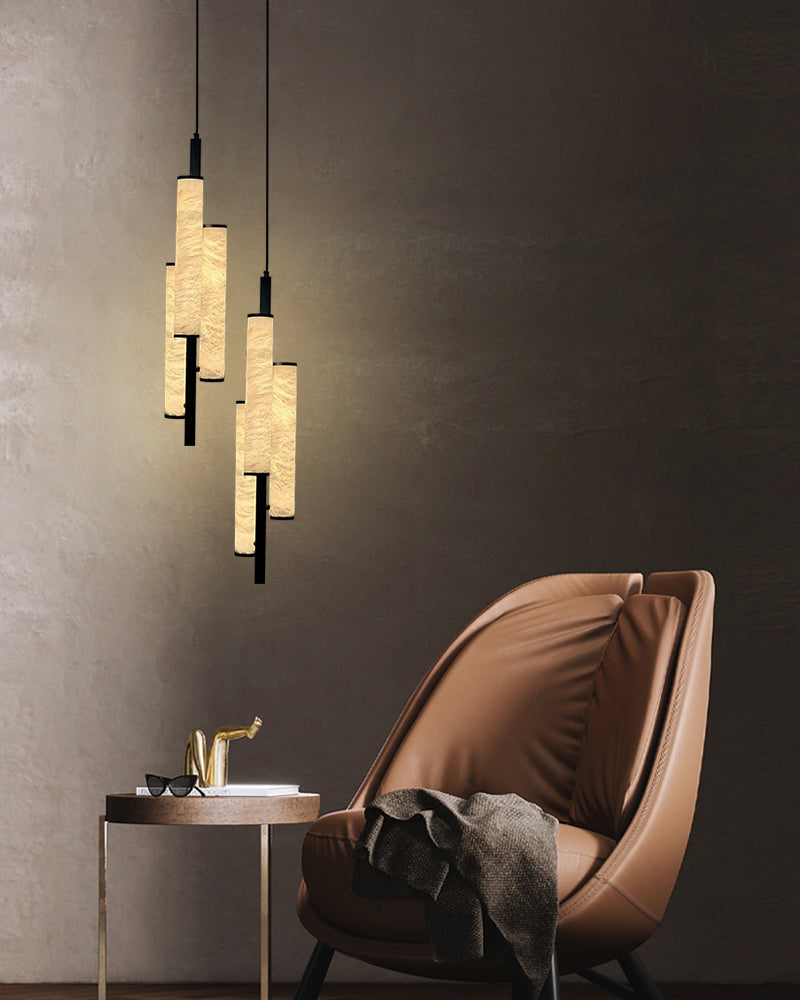 Three cylindrical alabaster pendant lamps above a modern brown armchair and side table.