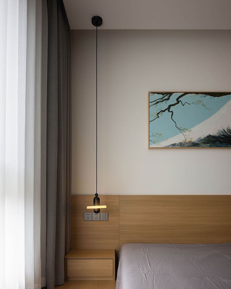 Modern black pendant lamp above minimalist bedside table in stylish bedroom.