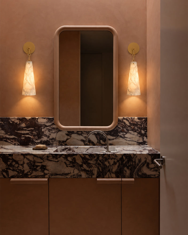 Conical alabaster wall sconce with metal backplate, warm light beside mirror