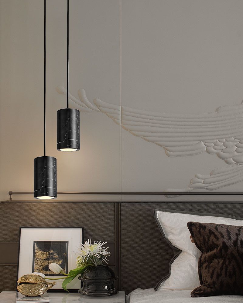Black cylinder pendant lamps above a bedside table in a modern bedroom setting