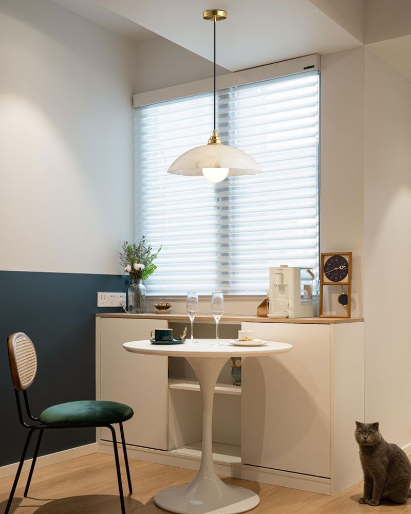 Minimalist dining area with round white table, green chair, and brass pendant lamp.