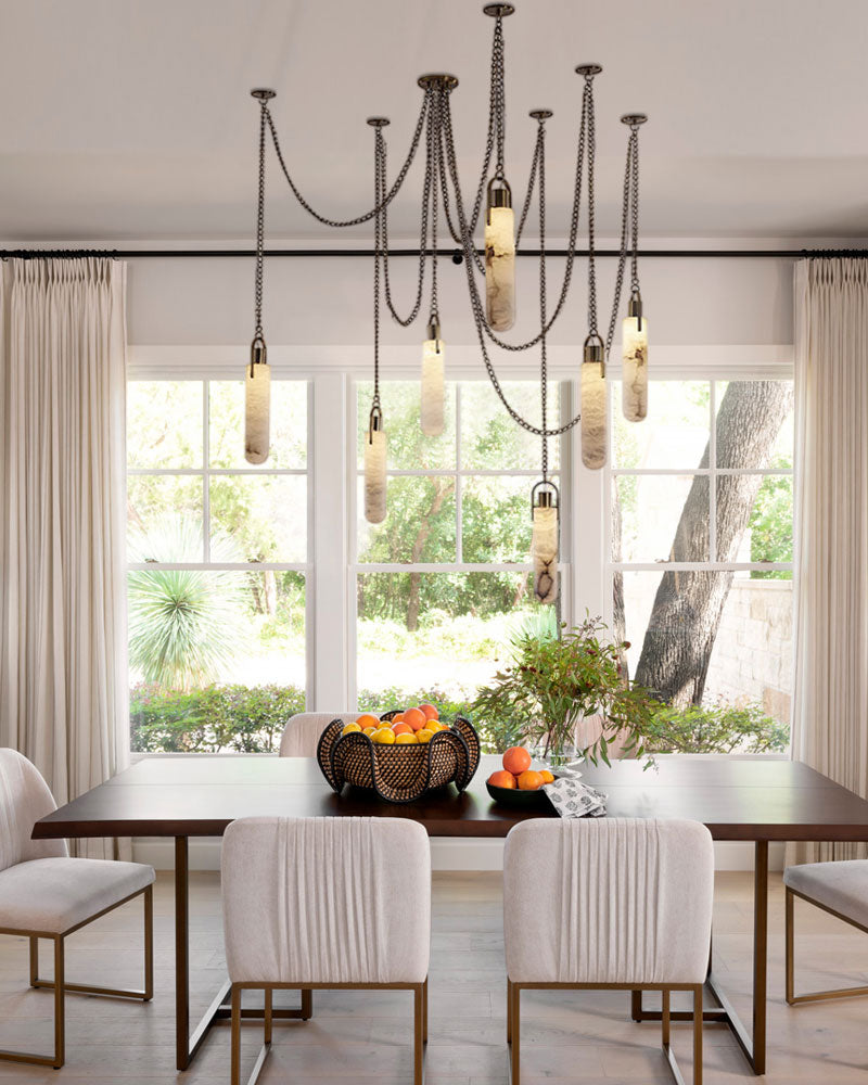 9-light brass LED pendant lamp over a wooden dining table in a bright, modern dining space.