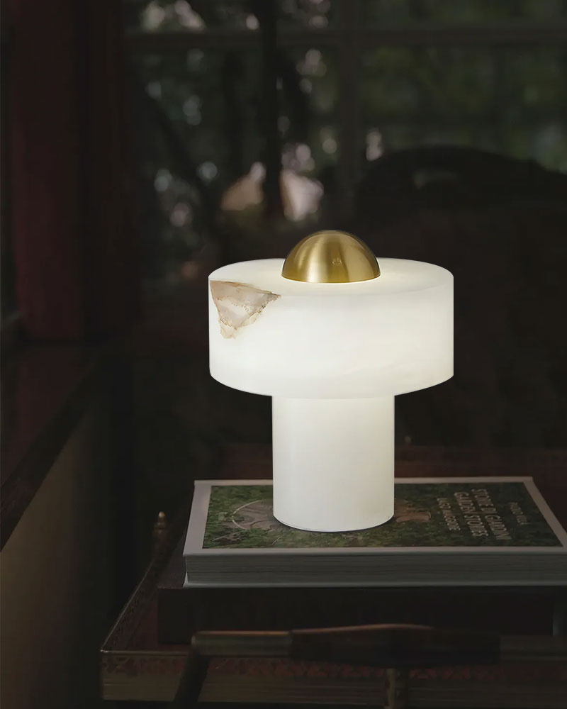 Stone alabaster table lamp with brass accent atop a stack of books in soft lighting