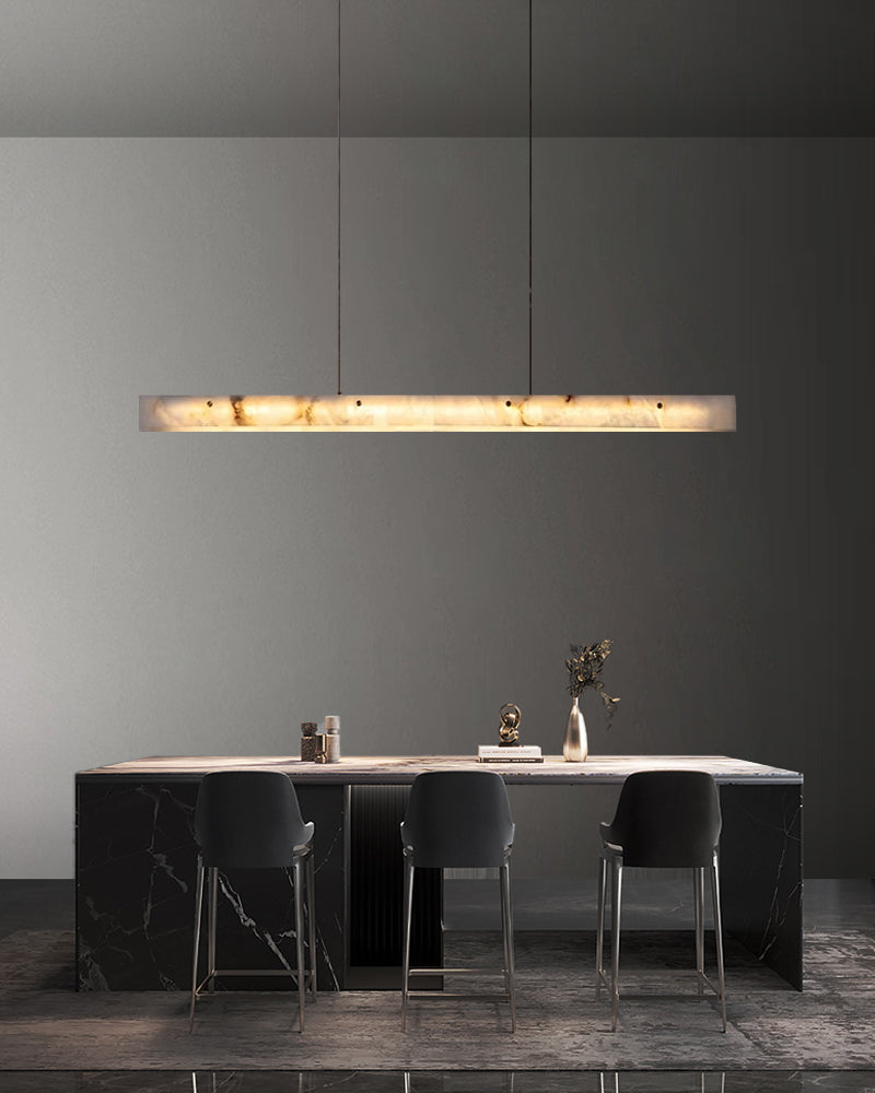 Long marble pendant light illuminating a minimalistic kitchen island with black stools.