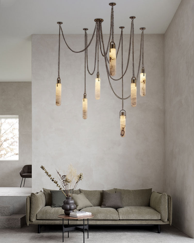 Brass LED cluster pendant lamp above a cozy olive green sofa in a bright, modern space.