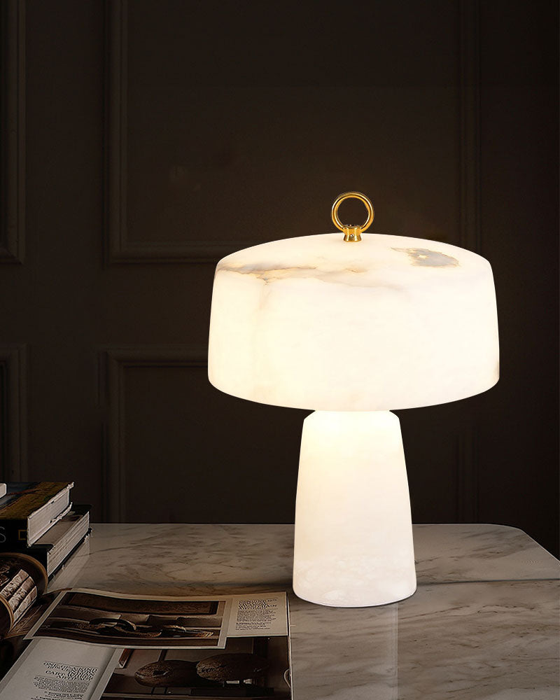 G9 cloud stone table lamp with gold accent on sleek marble table beside books.