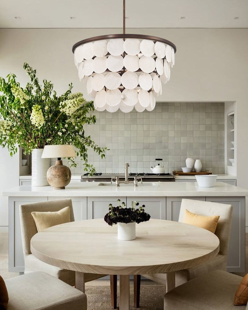 A modern tiered pendant chandelier with white circular glass discs hangs over a round dining table in a bright, contemporary kitchen and dining room setting.