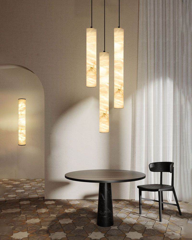 Alabaster cylindrical pendant lamps above a round black table in a minimalist room