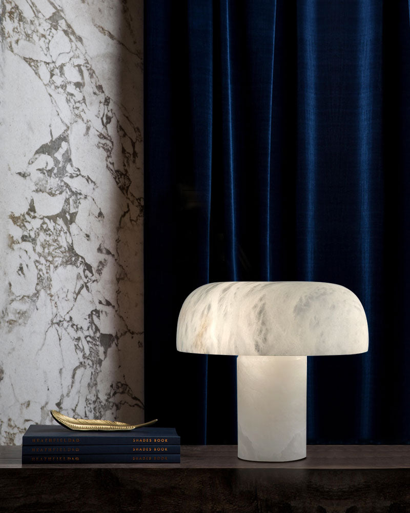 Modern white marble table lamp with rounded shade on a wooden table near decorative books.