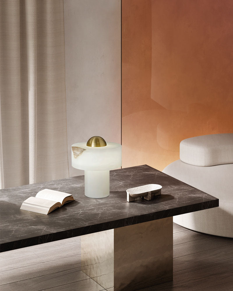 Stylish alabaster table lamp with brass accent on a marble table beside an open book.