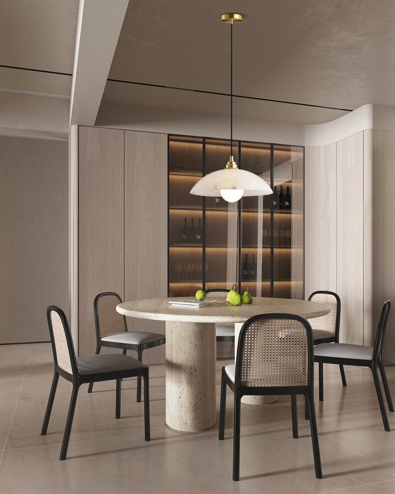 Contemporary dining area with round stone table, black chairs, and brass-accented pendant.