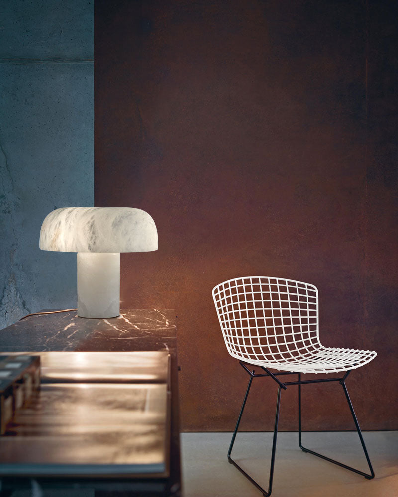 Stylish white marble table lamp beside modern wire chair on wooden table.