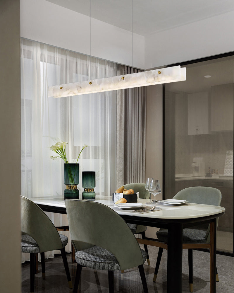 Minimalist marble pendant light above a round dining table with green chairs in a chic setting.