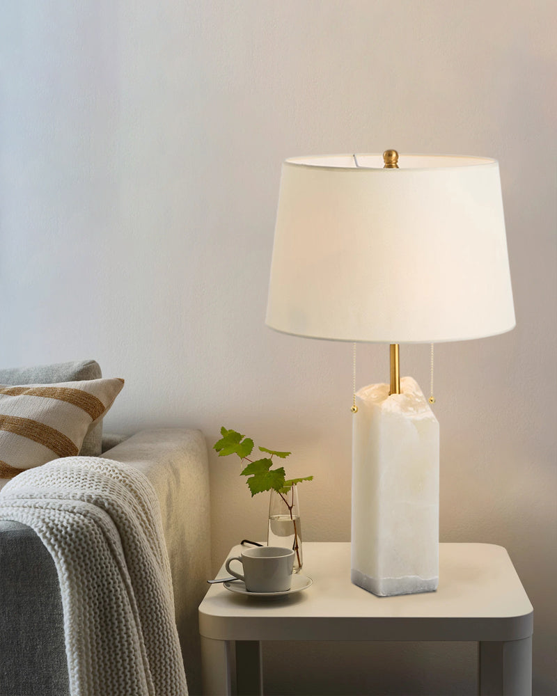 White alabaster table lamp with linen shade on a side table beside a sofa