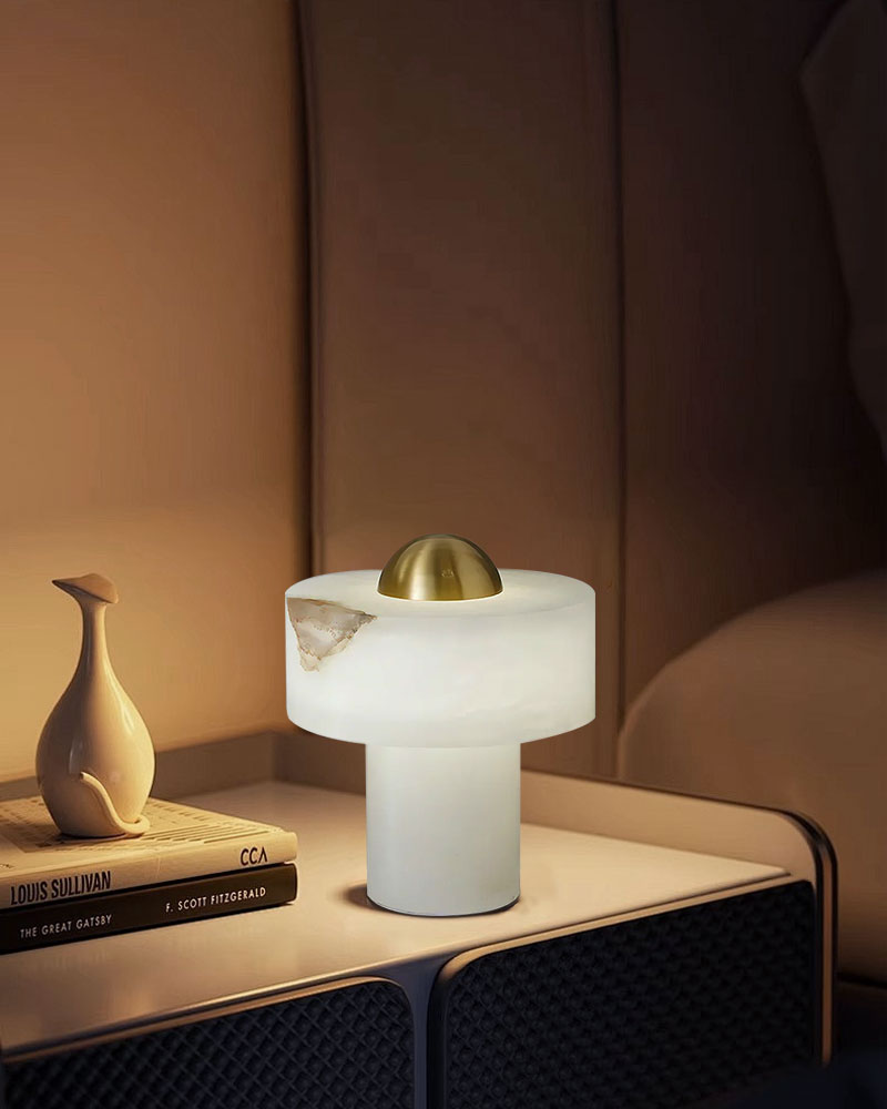 Modern alabaster table lamp with brass accent on a nightstand beside a decorative vase.