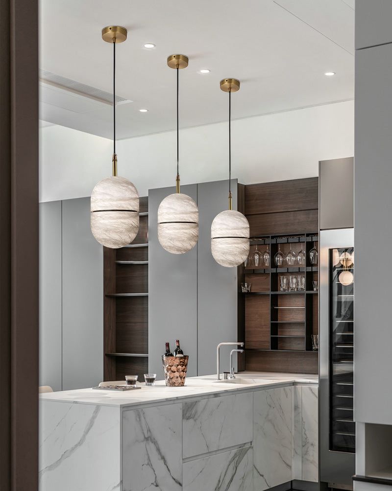 Three alabaster pendant lights illuminating a sleek kitchen island with marble countertop