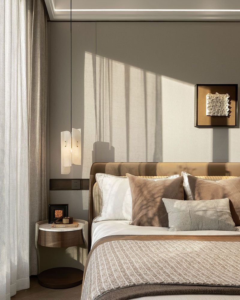 Elegant bedroom with beige bed, soft cushions, and alabaster pendant lighting.